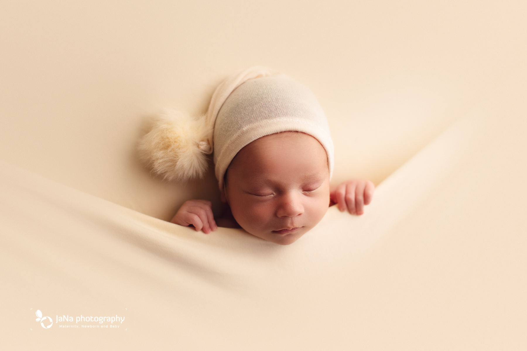 newborn baby boy sleeping on a cream background wearing hat