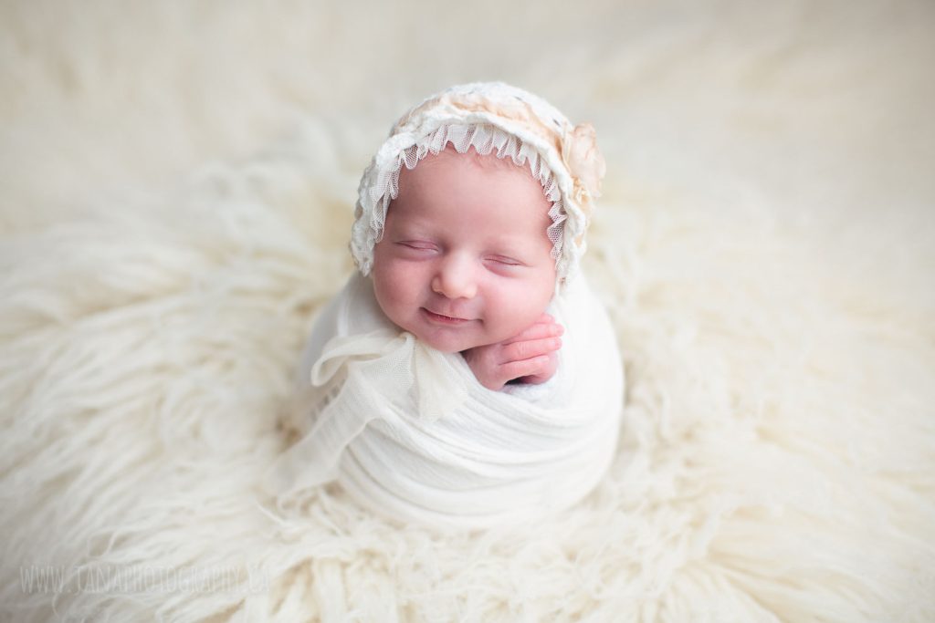 newborn baby girl in a white setup fur smiling