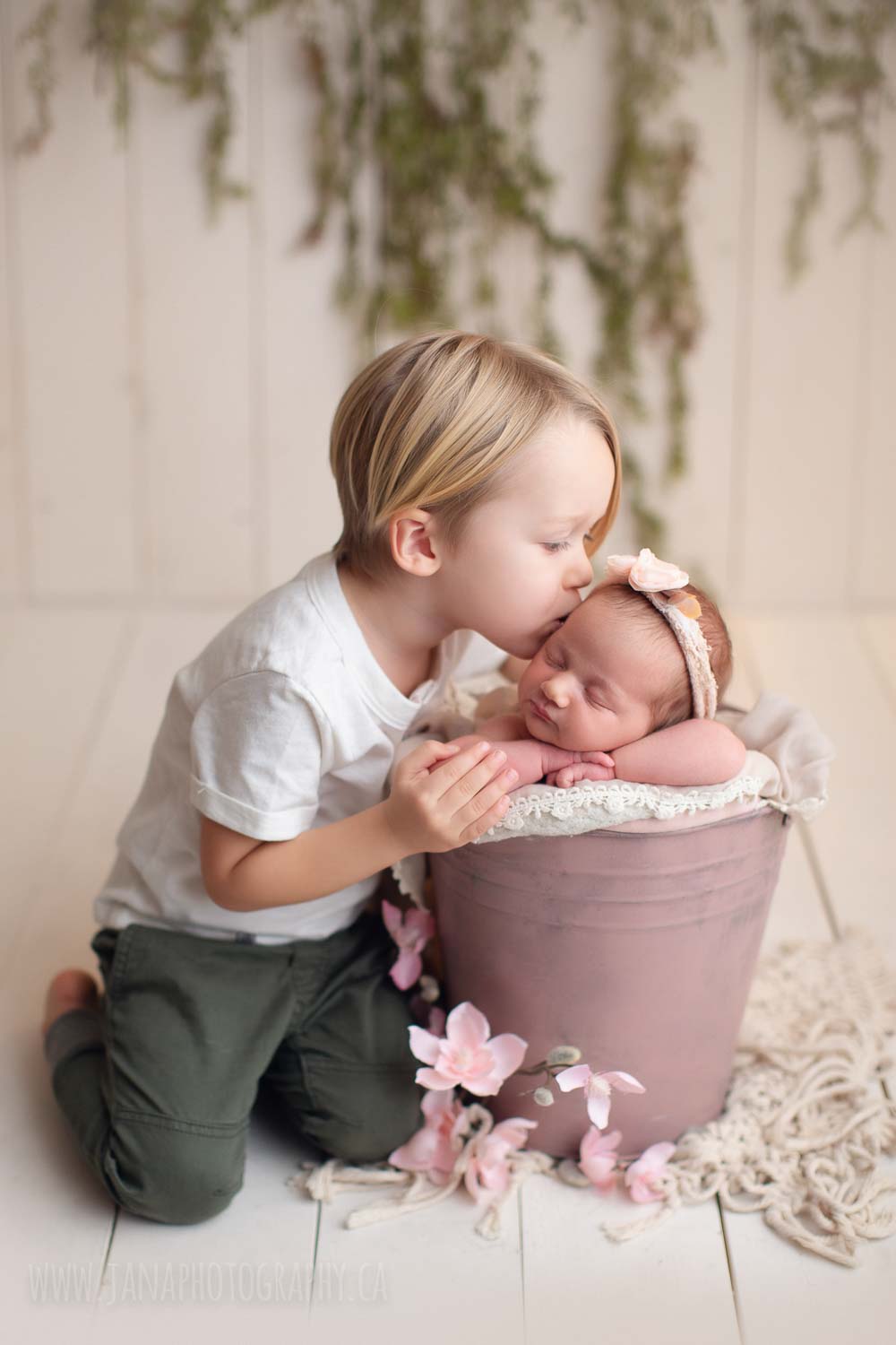 baby brother is kissing newborn girl sister in a pink bucket