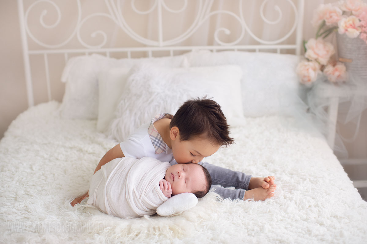 baby brother is kissing his newborn baby - natural light bed