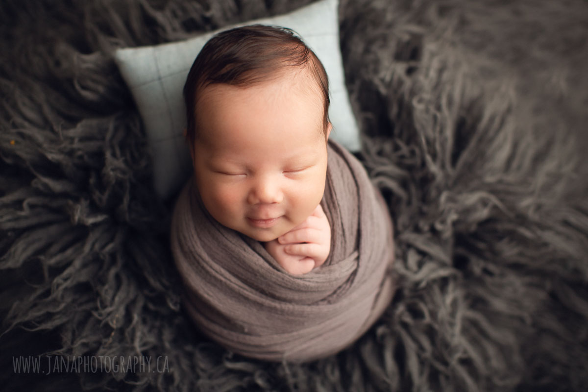 newborn baby boy in a grey background smiling - vancouver bc