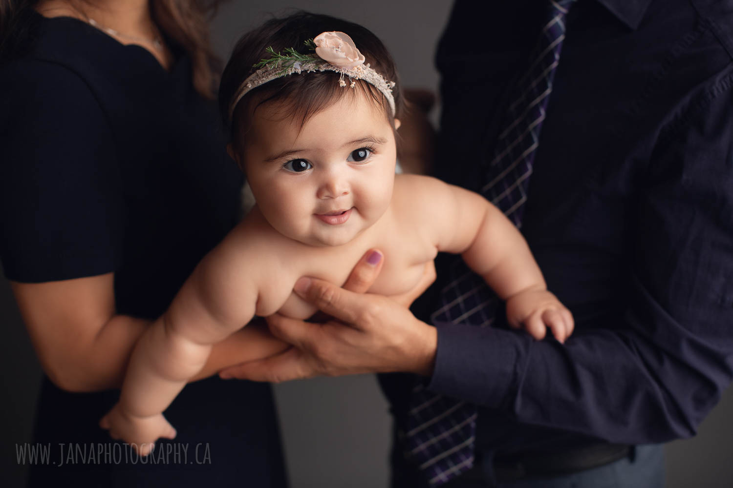 Baby girl smiling in her parents hands looking at the camera