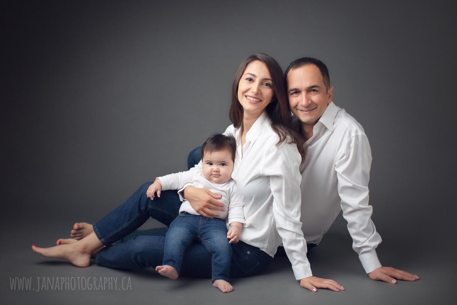 Parents with 6 month baby girl sitting with white shirts and black background