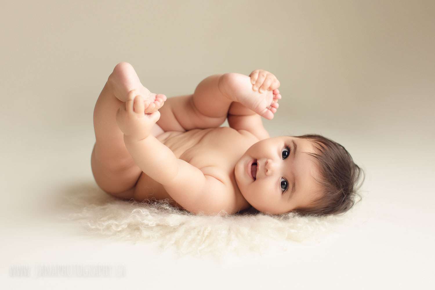 Six month old baby girl naked holding her feet