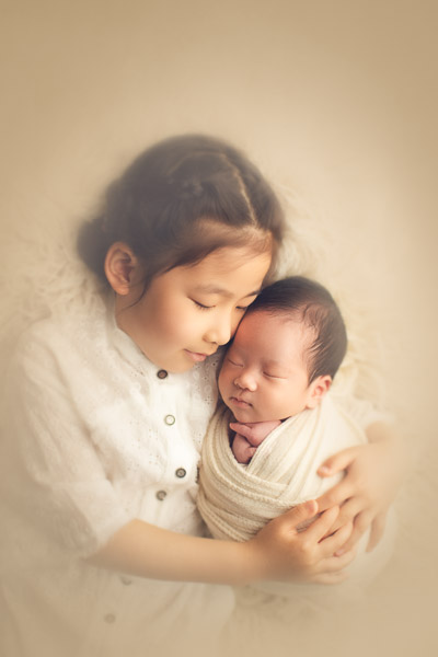 newborn photography sister hugging her brother in cream background