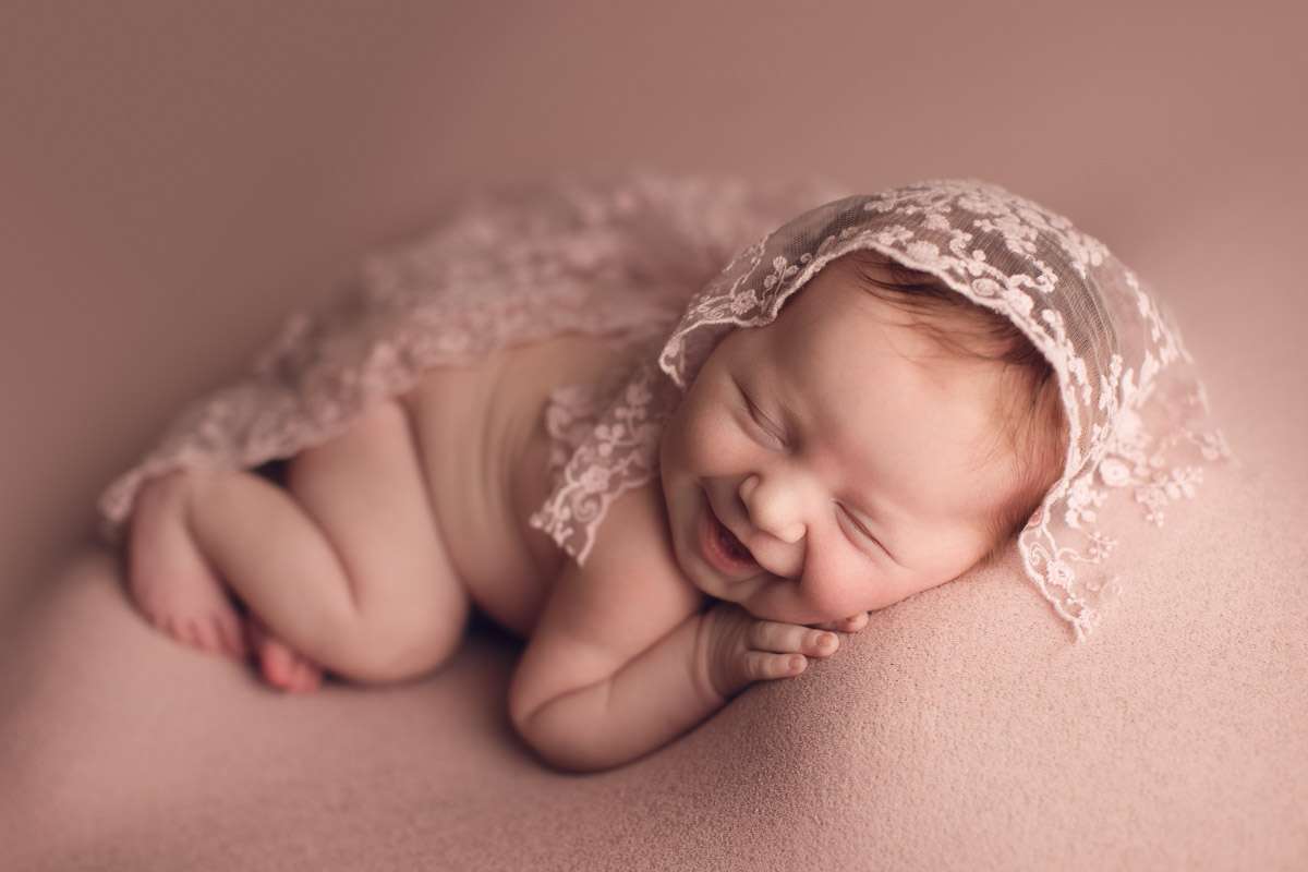 newborn baby girl smiling in a pink background