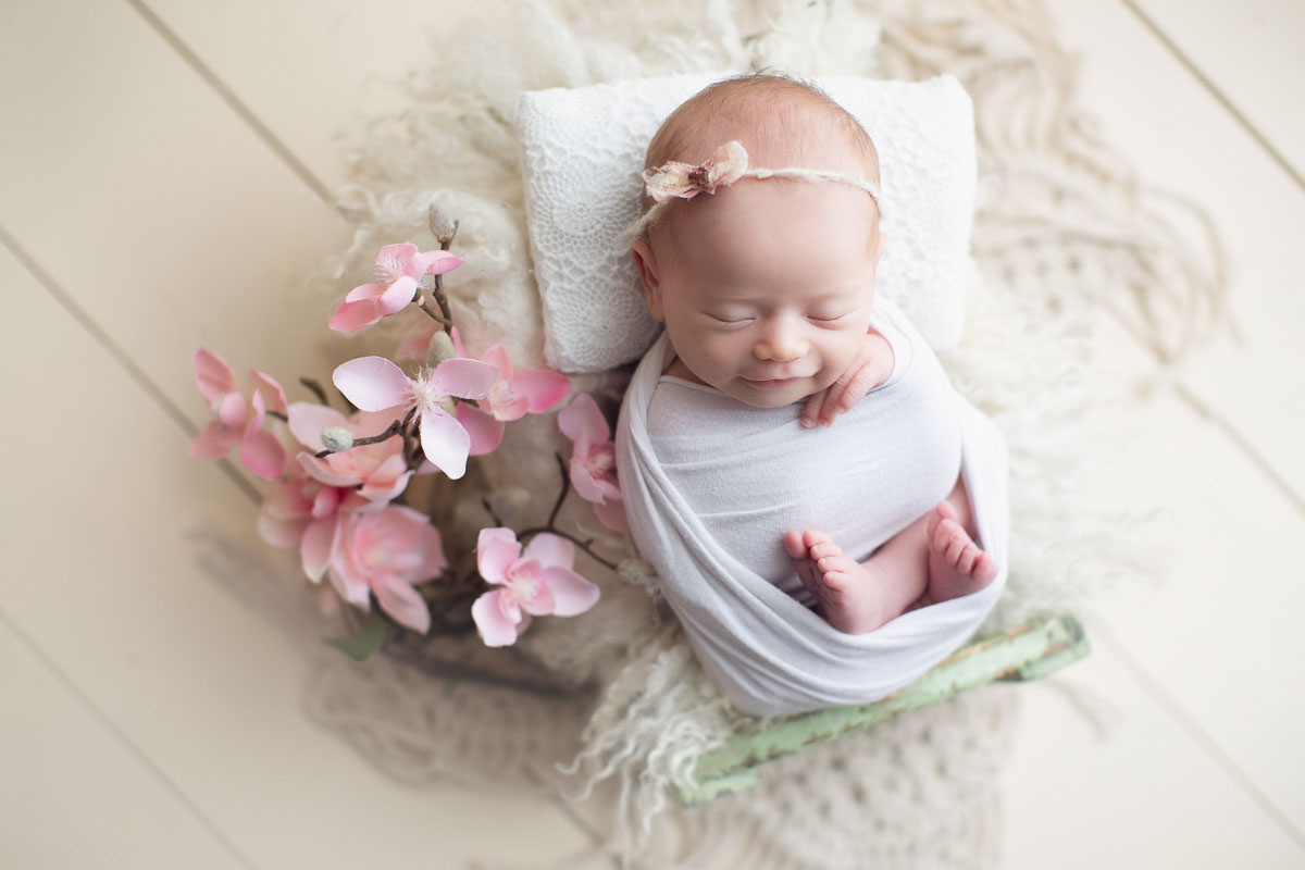 newborn baby girl smiling in a white wrap and flower
