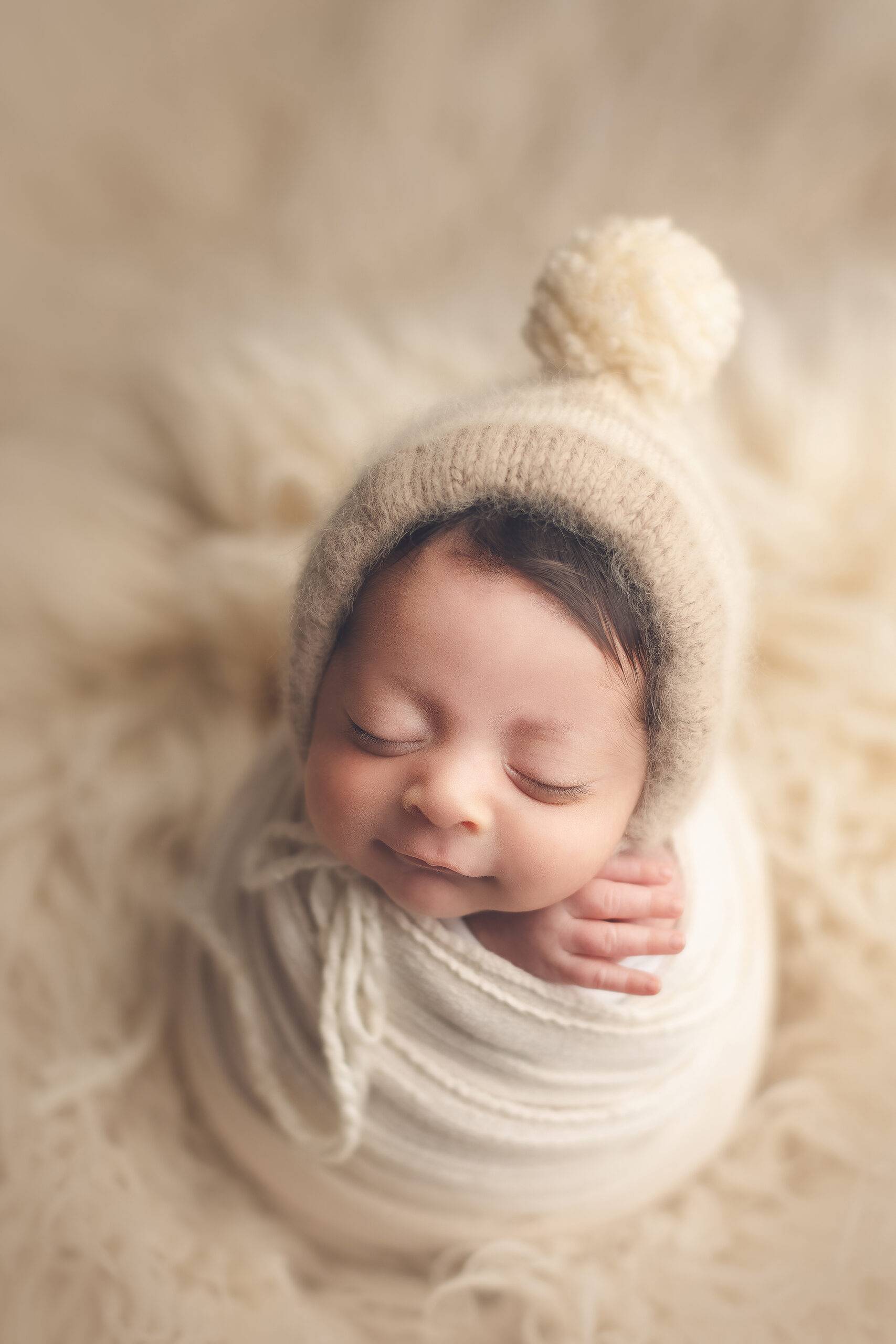 newborn baby boy smiling with a white wrap and hat
