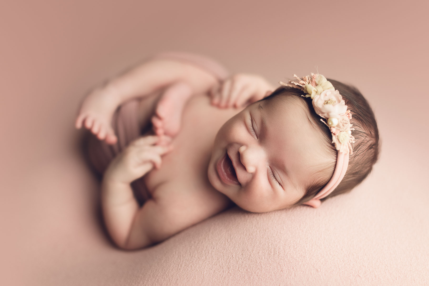newborn photography baby girl on pink background smiling with floral head band - vancouver-burnaby -surrey