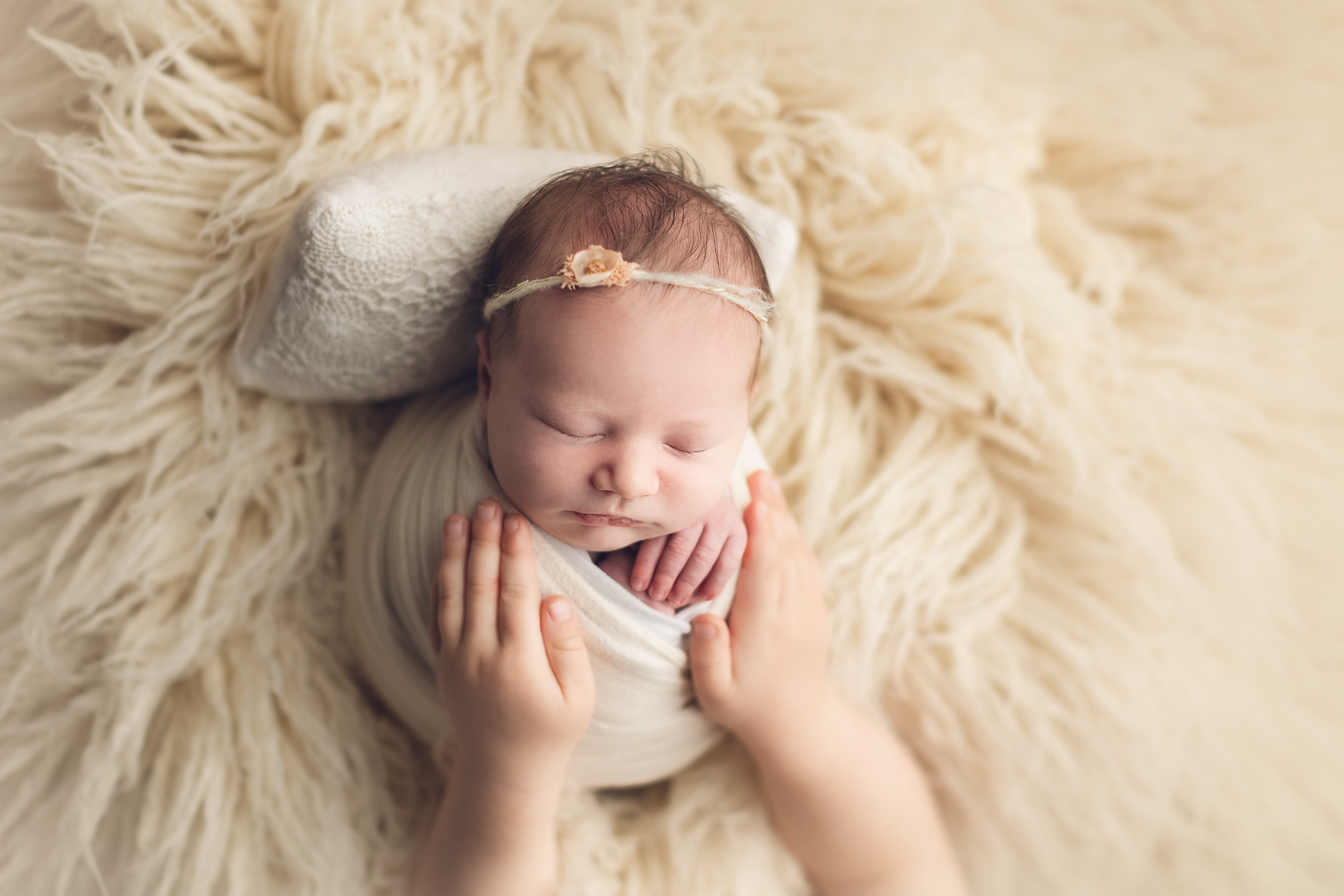 her sister is holding newborn baby in a white fur. best newborn photographer in vancouver