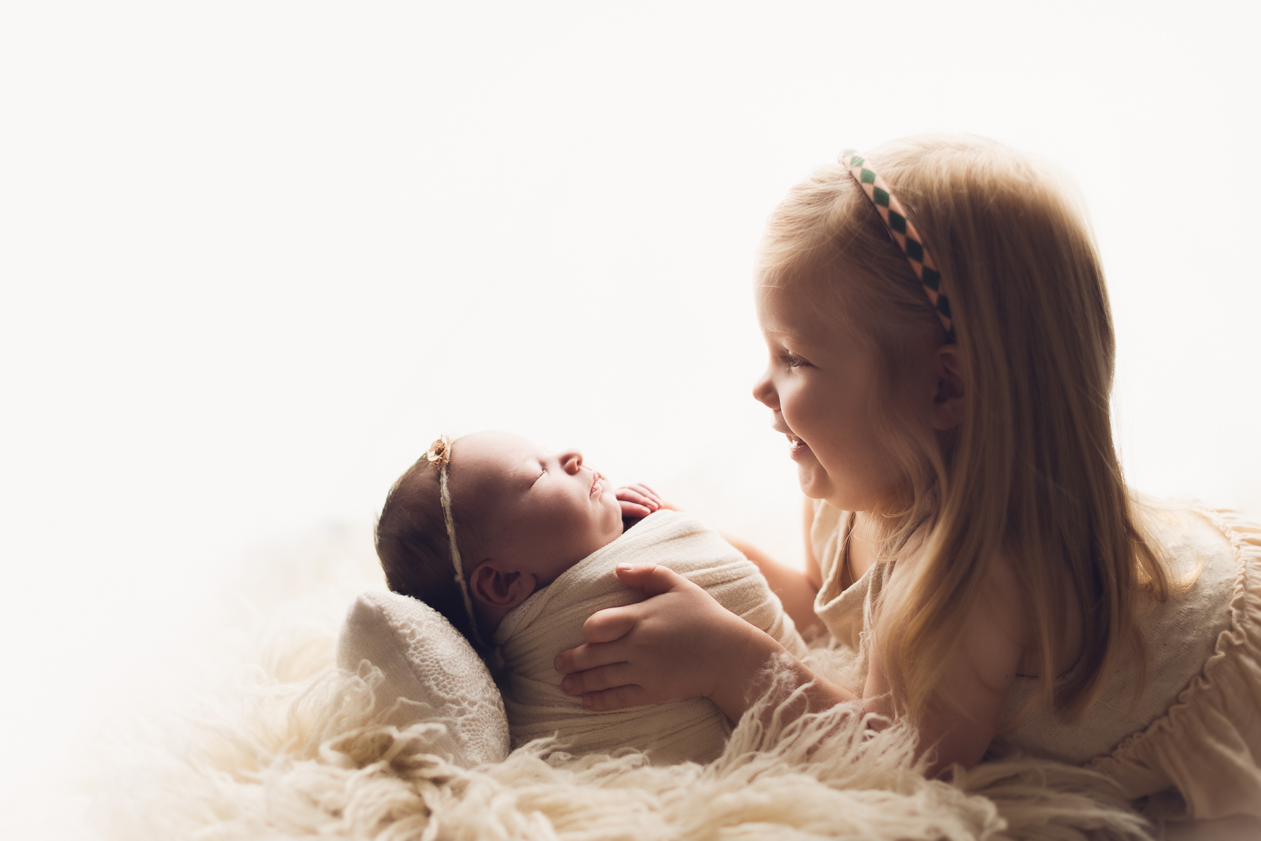 sibling and newborn photography in white fur. smiling picture, newborn photography near me