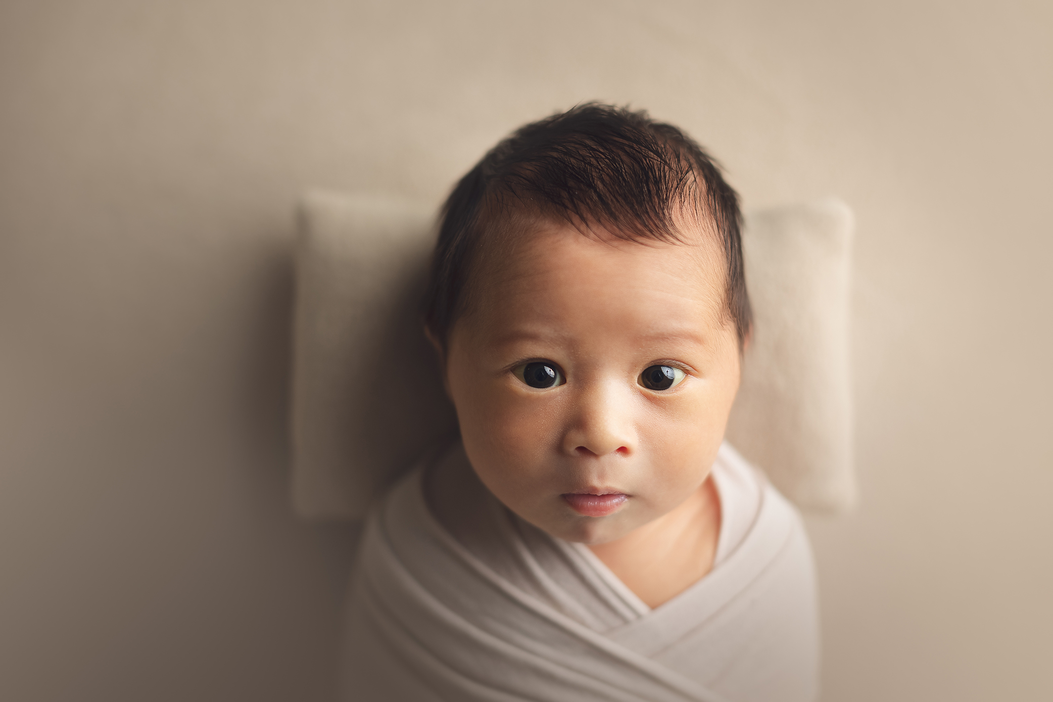 newborn baby boy with open eyes in a cream background