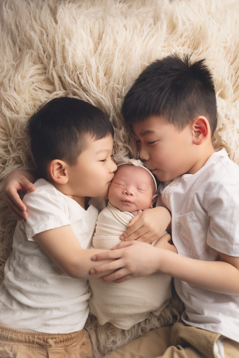 brothers kissing their sisters in white background and studio lighting - jana in the best newborn photographer