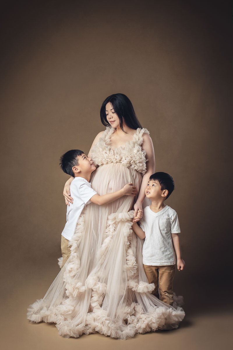 pregnant mom is standing with her 2 boys and smiling during their maternity photography session