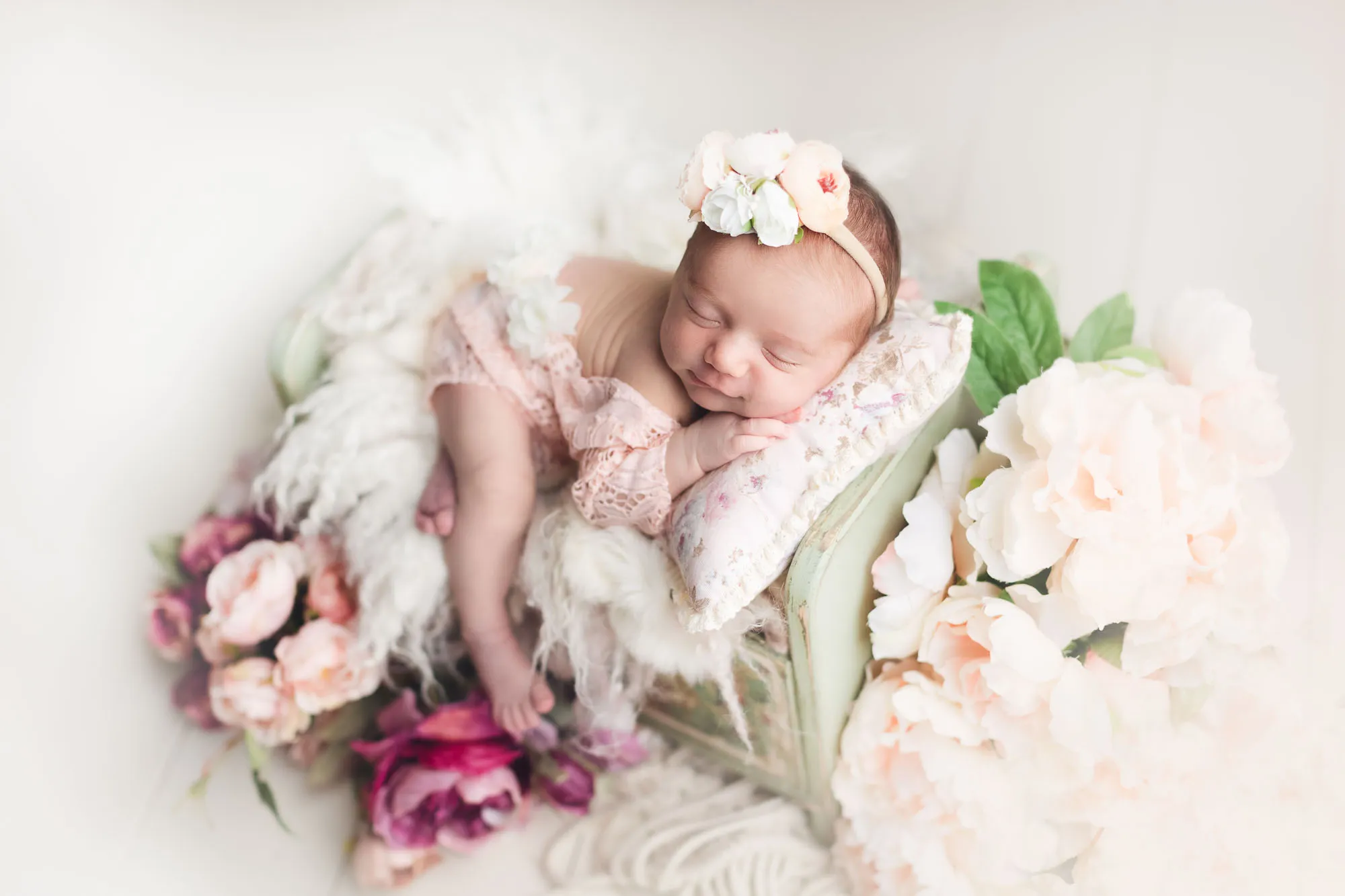 a newborn baby girl sleeping on a small bed with flowers
