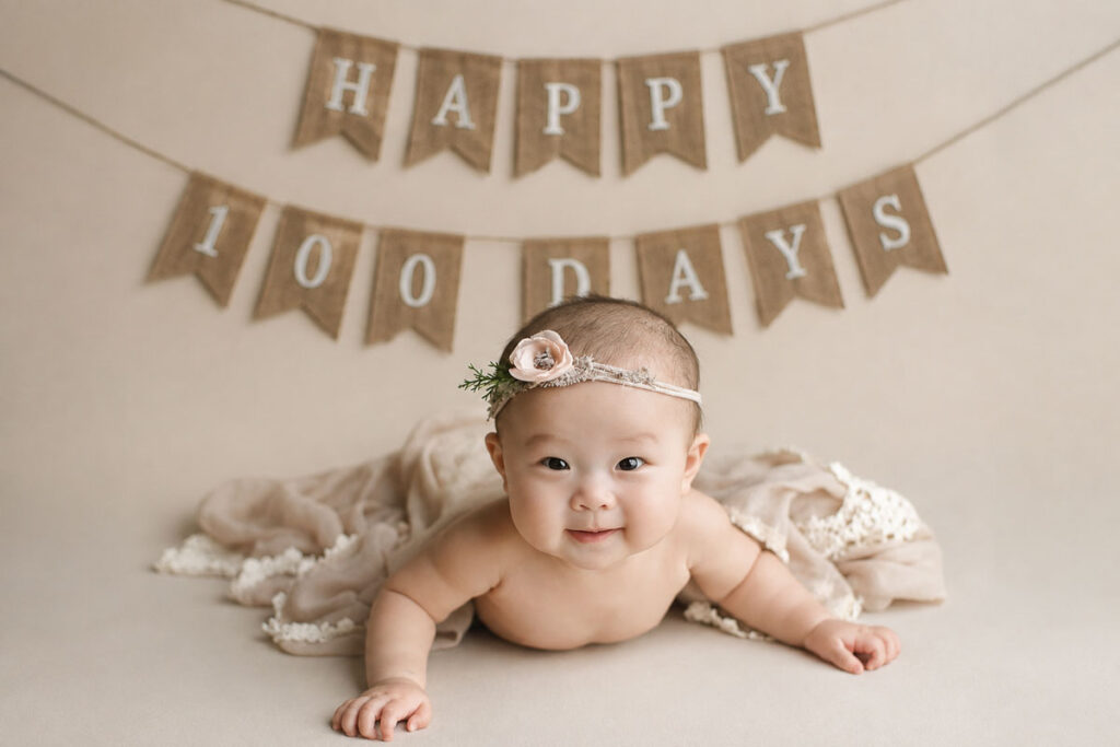 Baby smiling on tummy for 100 days photography session in Vancouver, happy 100 days banner in background